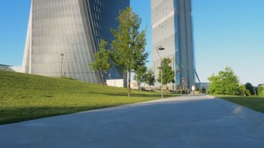 Milano 'nun Citylife semtindeki küçük bir yolun zemin perspektifinden kamera hareketleri ve güneşli bir günde arka planda modern gökdelenler. Kamera yukarı.
