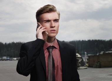 Genç sarışın adam elinde telefonla konuşuyor ve ileriye bakıyor. İş kavramı