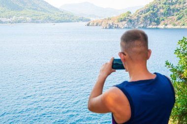 Genç beyaz turist seyahat dağ ve deniz onun celephone fotoğraf çekmek