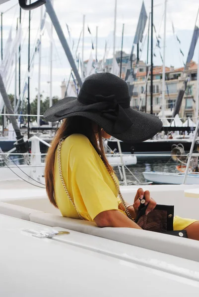 Lady in big black hat and long hair at the pier of yachts