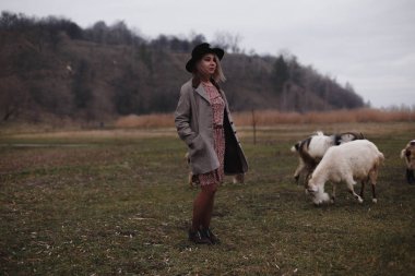 Şapka ve keçilerle sahada tek başına duran kadın. Kadın çiftçi