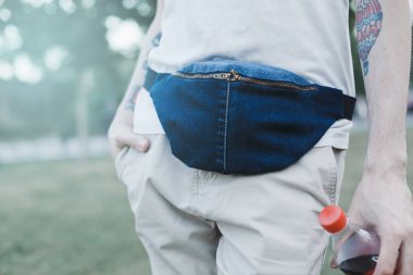 Genç dövmeli adam trendy mavi şık kemer denim çanta debriyaj. Kentsel sokak stili