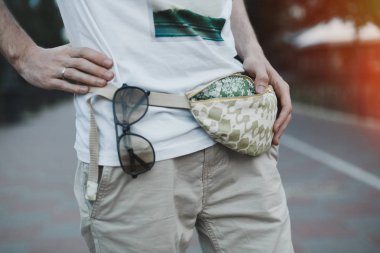 Trendy bej şık kemer pamuk torba debriyaj güneş gözlüğü ile genç adam. Kentsel sokak stili