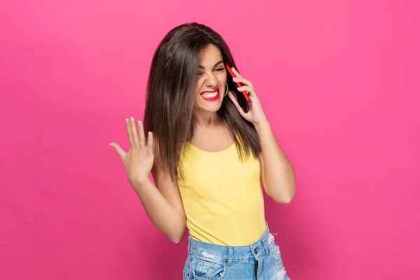 Nervous brunette talking on a cell phone and screaming into a phone on a pink background