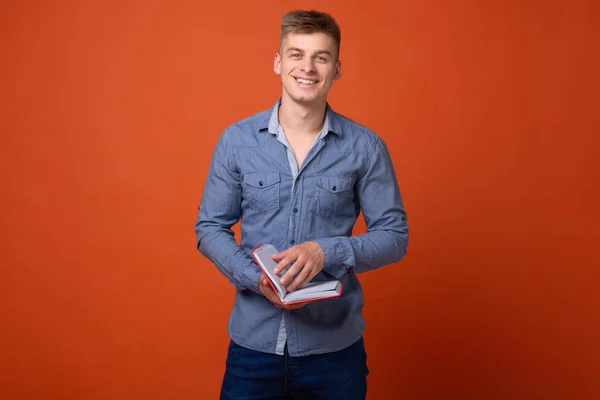 young man with book smiles on orange background in studio