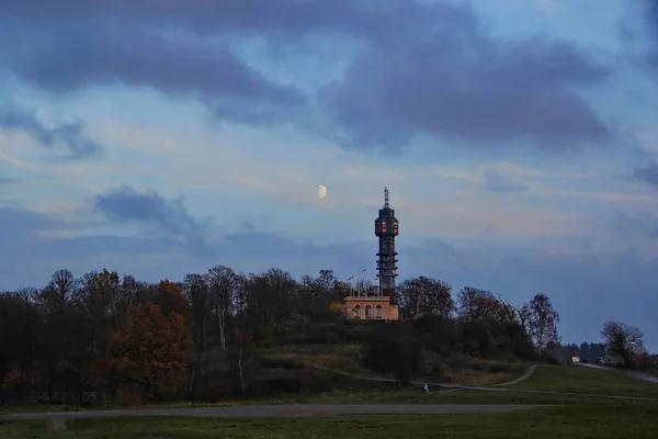 Üstünde belgili tanımlık tepe gece karanlığında kule. Sonbahar orman. Ay gökyüzünde.