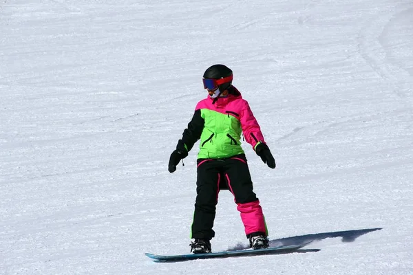 Girl in a colorful suit is on a snowboard rides with mountains — Stock Photo, Image