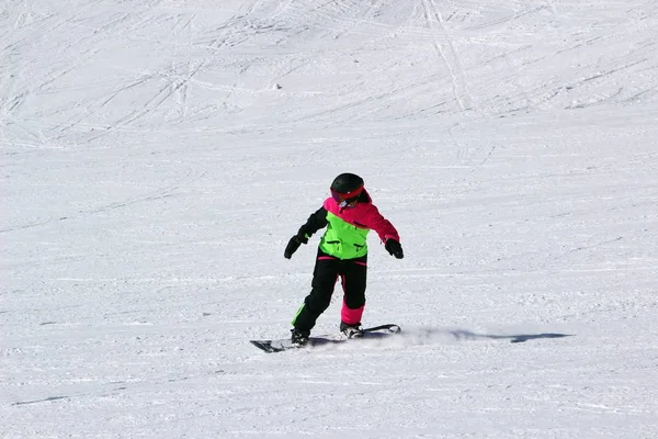 Mädchen im bunten Anzug ist auf einem Snowboard mit Bergen unterwegs — Stockfoto