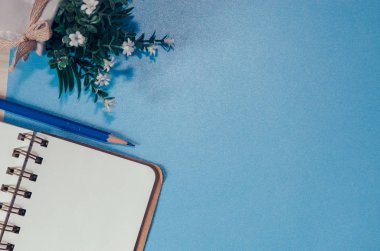 Mavi bir arka plan üzerinde kopya alanı, boş defter, kalem ve ağaç tencere ile üstten görünüm