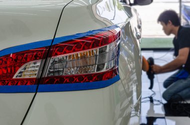 El ele tutuşan bir adam arabanın kaputunu ve beyazını parlatıyor. Arka lambaya odaklan.