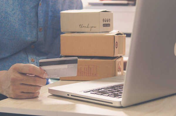 Мужские руки держат кредитную карту и коробку посылку и ноутбук за столом..