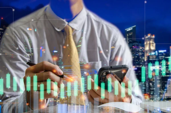 Double exposure financial graph and businessman using smartphone and pen with cityscape on blurred building background.