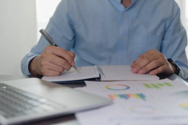 Odaklanmış iş adamı finansal veri tablolarıyla iş stratejisi yazıyor. Analiz ve karar alma için ofis çalışma ortamı.