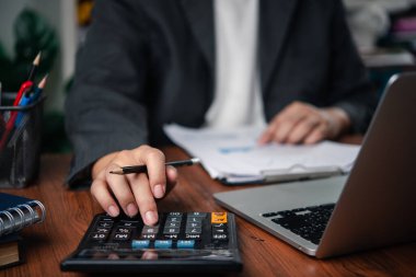 İş adamı, mali verileri evrak ve dizüstü bilgisayarla analiz ediyor, hesaplama, harcama yönetimi ve finansal raporlama gösteriyor. Muhasebe, bütçe ve vergi planlama