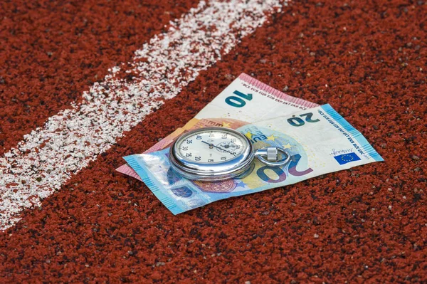 old sport stopwatch and money on running track rubber