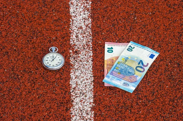 old sport stopwatch and money on running track rubber