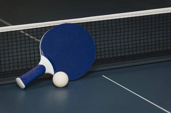 Raquetas de tenis de mesa y pelota y red sobre una mesa de ping pong azul — Foto de Stock