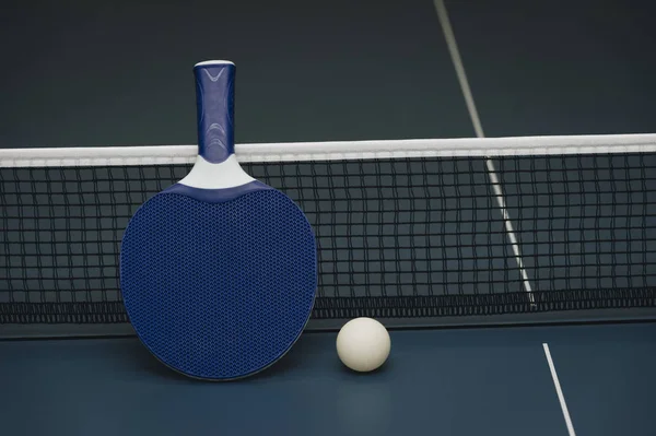 Raquetas de tenis de mesa y pelota y red sobre una mesa de ping pong azul — Foto de Stock