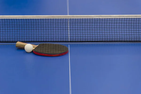 white ball for table tennis lies on a blue table with net on background