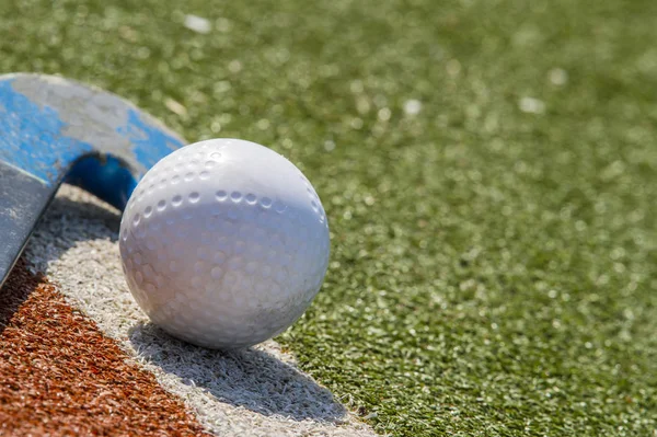 Field hockey stick and ball on brown and green grass