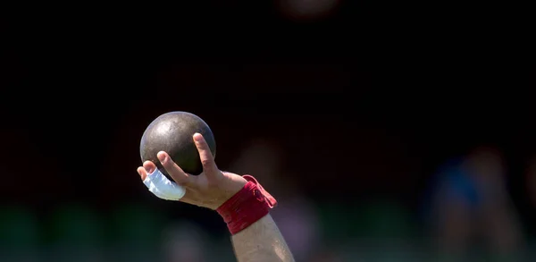 Man Lifting Shot Put at a Track and Field Meet