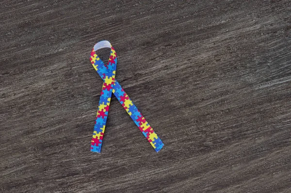 World Autism awareness and pride day or month with Puzzle pattern ribbon on wooden background.