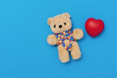 Dünya Otizm Farkındalık günü, ruh sağlığı kavramı. Kırmızı kalp ve kurdele bulmaca desenli oyuncak ayı. Mavi arka planda