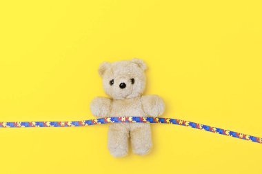 Dünya Otizm Farkındalık günü, oyuncak ayı ve kurdele bulmaca desen ile ruh sağlığı kavramı. Sarı backgroun üzerinde