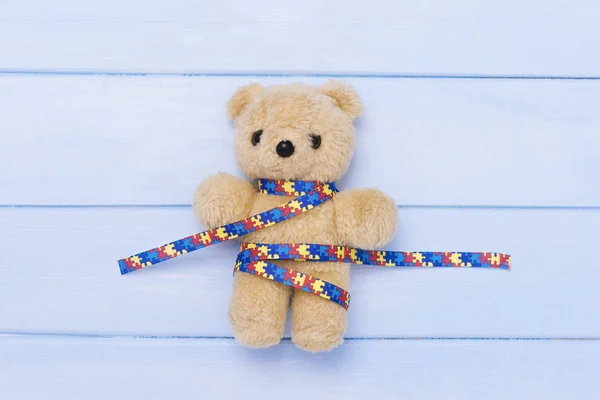 World Autism Awareness day, mental health care concept with teddy bear and ribbon puzzle pattern. On blue backgroun