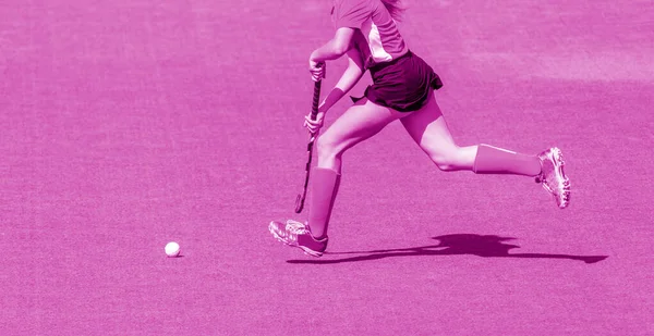 Young hockey player woman with ball in attack playing field hockey game. Pink color filter