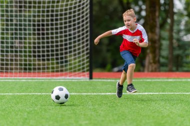 Çocuklar için futbol antrenmanı. Çocuk koşuyor ve futbol topunu tekmeliyor. Genç çocuk futbol becerilerini geliştiriyor.