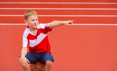 Çocuk, kırmızı sahada basketbol topuyla poz veriyor. Sahada spor eğitimi. Çocuk sporu online konsepti