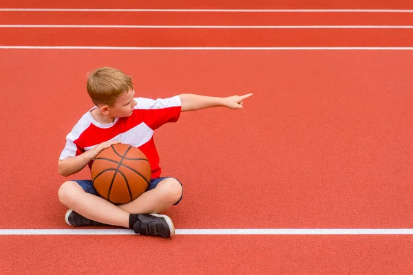 男孩在人造的红色草皮上摆着篮球的姿势 该领域的体育培训 儿童体育在线概念 — 图库照片