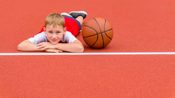 男孩在人造的红色草皮上摆着篮球的姿势 该领域的体育培训 儿童体育在线概念 — 图库照片