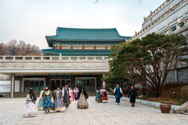 Seoul, South Korea - Dec 25,2025: Groups in colorful hanbok walk outside the National Folk Museum of Korea in Seoul, with traditional blue-roof architecture in the background.