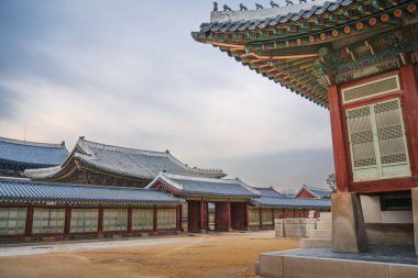 Detailed view of Gyeongbokgung Palace courtyard in Seoul with ornate tiled roofs, red wooden walls, and intricate dancheong patterns.