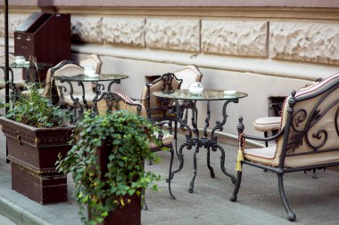 Dövme demir içeren bir tablo bacaklar ve sahte sandalye ve binanın cephe çerçevede sokak kafe terasında yumuşak koltuk ile cam masa üstü.