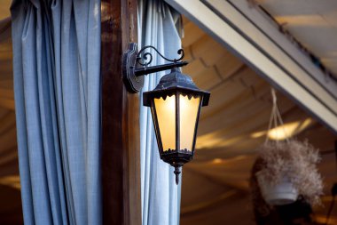 gazebos ve terasların dövme demir, mavi perde kıvrımlar Tartı ile kahverengi bir ayağı üzerinde aplikler için dekoratif fener.