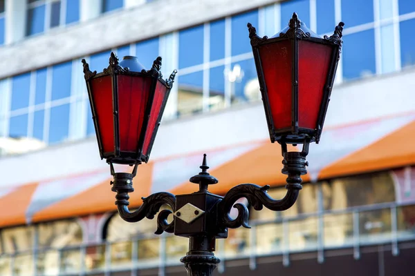 Street lamp lighting forged from metal in black and red glass, a lantern against the background of the facade of the building close-up.