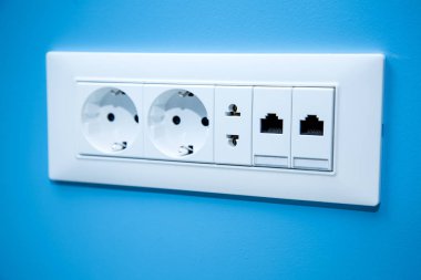 Socket electrical outlets for electrical plugs and electricity a set of different types of power connectors for European and American stanlart and connect the Internet cable close-up on the blue wall. clipart