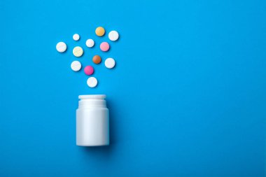 Çeşitli renk tabletleri grubudur. Beyaz şişeden dökülmesini hapları. mavi arka plan. kavramsal arka plan metin kopyalama yeri olan nesneleri en iyi manzaralı bir tıbbi Sanayi.