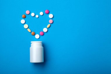 Metin için özgür kopya yer ile mavi bir arka plan üzerinde bir kalp şeklinde renkli hapları ile kardiyoloji Tema plastik beyaz şişe kavramı.