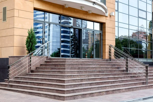 stone steps with a handrail on the side of the climb to the glass doors of the business center.