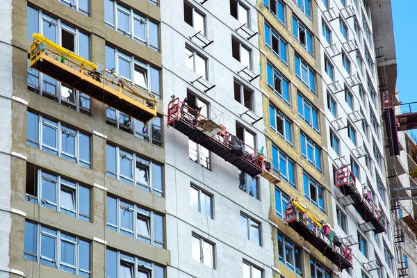 Construction cradles perform facade work on the weatherization and painting of a skyscraper under construction.