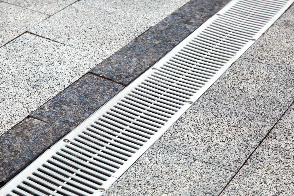 metal gutter on a pedestrian sidewalk of decorative stone tiles close-up.