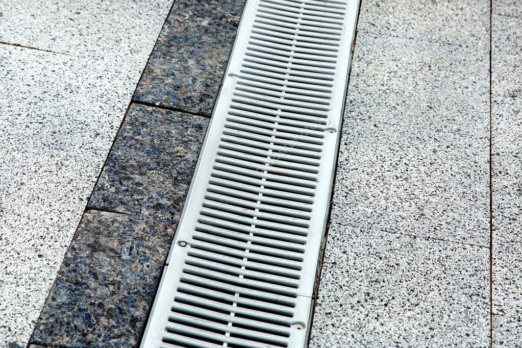 metal gutter on a pedestrian sidewalk grey tiles close-up.