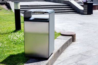 Metal bir kare açık çöp tenekesi kaldırıma Yaya kaldırım taş döşeme arka planı merdivenleri arasındaki bir çim yeşil çim ile yüklü.