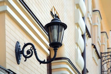 Siyah demir duvar lambası sarı tuğla bina cephesinde monte.