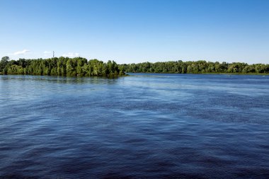 Manzara nehir sahile mavi gökyüzüne karşı yeşil ağaçlar ile arka plan üzerinde koyu mavi su ile.