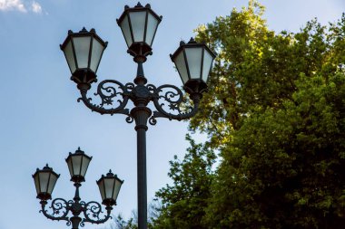 Sokak lâmbası direği desen ve cam ile üçlü bir fenerle eklemek park görünümünde aşağıdan ağaçlar ve gökyüzü arka planı.